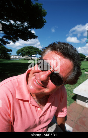 Diese glücklichen männlichen Urlauber in ein Lachs rosa Polo-Shirt und eine Sonnenbrille sitzt und wartet, genießen Sie die warme Sommersonne Stockfoto