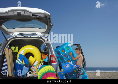 Junge (10-12) entladen Luftmatratze von Auto voller Strand-Accessoires Stockfoto