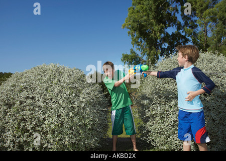 Zwei Jungs (6-11) spielen mit Wasserpistolen unter Büschen, lachen Stockfoto