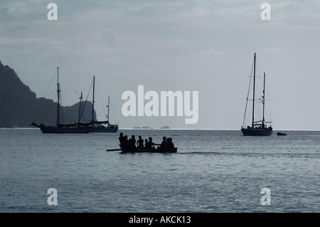 Yachten in der Abenddämmerung vor einer Karibik-Insel und Menschen Rudern ein Schlauchboot in der Bucht verankert Stockfoto