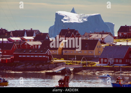 Typische grönländischen Häuser in Kontrastfarben mit riesigen Eisberg über bei Qeqertarsuaq auf Westküste von Grönland Stockfoto