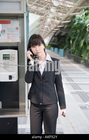 Geschäftsfrau, die auf ein öffentliches Telefon auf einem Flughafen im Gespräch Stockfoto