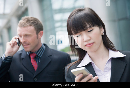 Eine Geschäftsfrau mit einer personenbezogenen Daten-Assistent mit einem Geschäftsmann telefonieren mit einem Handy hinter ihr in Nahaufnahme Stockfoto