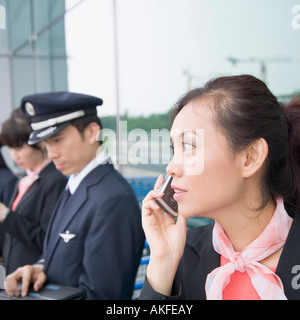 Nahaufnahme von einem weiblichen Flugbegleiter sprechen auf einem Handy mit einem Piloten mit einem Laptop im Hintergrund Stockfoto