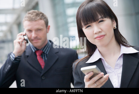 Eine Geschäftsfrau hält eine Daten-Assistent mit einem Geschäftsmann telefonieren mit einem Handy hinter ihr in Nahaufnahme Stockfoto