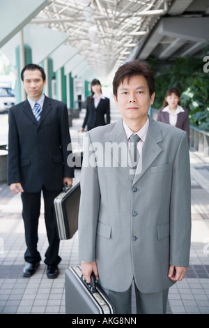 Unternehmer stehen und hält seinen Koffer mit drei Geschäftsleute im Hintergrund Stockfoto