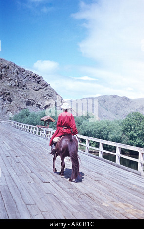 einsamer Mann Reiten auf Pferd wieder über eine Brücke, die Mongolei 1965 gebleicht Folie Stockfoto