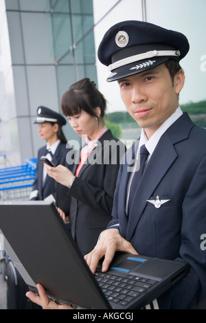 Seitenansicht von einer weiblichen Flugbegleiter halten eines Handys und stehen mit zwei Piloten am Flughafen Stockfoto