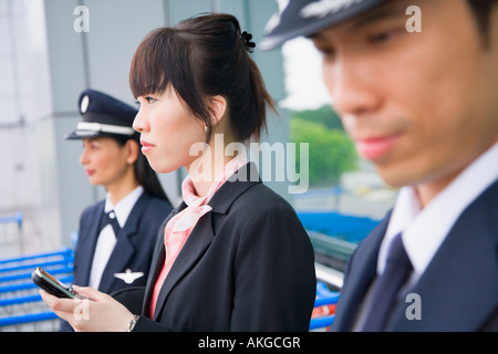 Seitenansicht von einer weiblichen Flugbegleiter halten eines Handys und stehen mit zwei Piloten am Flughafen Stockfoto