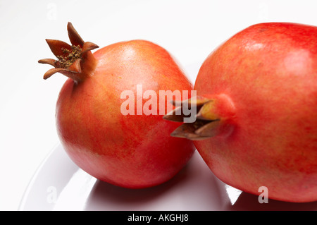 NAHAUFNAHME VON ZWEI FRISCHE GRANATÄPFEL AUF WEIßEN TELLER Stockfoto