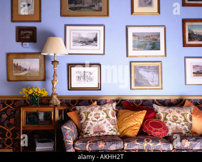 Gruppe von Bildern auf blauen Wohnzimmerwand über gemusterten Sofa mit bunten Kissen gestapelt Stockfoto
