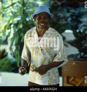 Lächelnd lokalen Mann in Sonnenhut und dekorative weiße Blumen tropischen Hemd spielen ein paar Maracas in Ocho Rios auf Jamaika Stockfoto