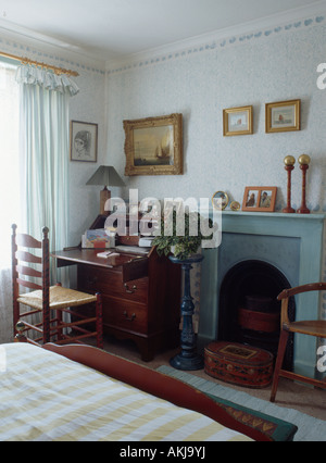 Antiker Schreibtisch und Rush Ladderback Stuhl in kleinen Schlafzimmer mit blassen blauen Kamin sitzen Stockfoto