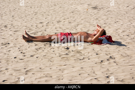 junger Mann mit Hochdruck daran am Strand Sonnenbaden genießen Sie die Sonnenstrahlen auf Backen sand Stockfoto