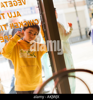 kleiner Junge in den indischen Café Fenster Hautpstraße Einzelhandel Southall West London suchen Stockfoto