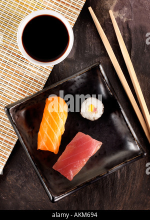 SCHWARZES QUADRAT-PLATTE MIT ZWEI STÜCKE VON ROHEM FISCH UND ZWEI KREISE VON VERPACKTEN REIS HÖLZERNE STÄBCHEN SCHWARZ TISCHPLATTE Stockfoto