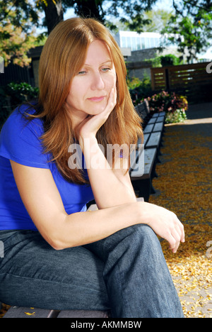 Reife Frau suchen traurig und gestresst sitzt auf einer Parkbank Stockfoto
