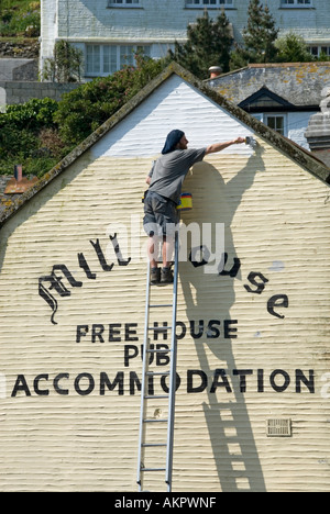 Polperro Rückansicht Mann bei der Arbeit lehnt sich von oben der Verlängerungsleiter Malerei Giebel Endwand des öffentlichen Hauses mit weißer Farbe Cornwall England UK Stockfoto