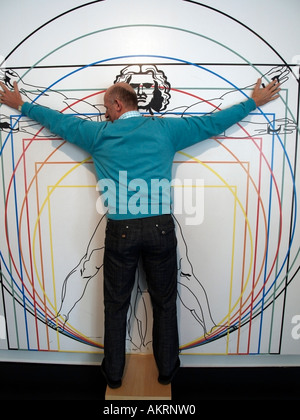 Mann, stehend mit Streched Arme an der Wand mit einer anatomischen Zeichnung nach Leonardo da Vinci im Museum Mathematikum Stockfoto