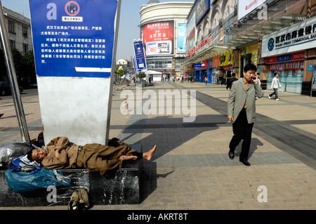 Ein Herumtreiber schlafen während ein Mann spricht mit Handy in eine Geschäftsstraße in Wuhan, Hubei China 21. Oktober 2007 Stockfoto