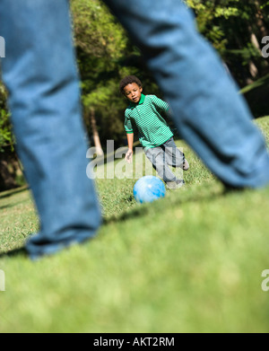 Sohn, laufen und treten Ball in Richtung Vater im park Stockfoto
