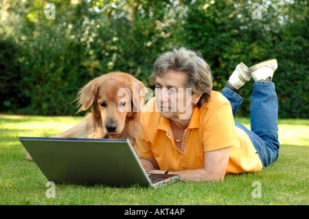 Ältere Frau mit Laptop und Hund auf einer Wiese Stockfoto