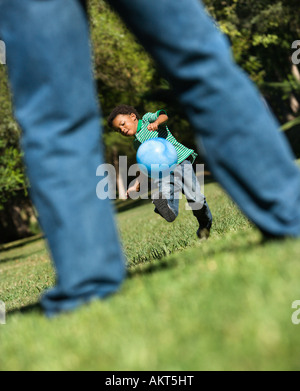 Sohn, laufen und treten Ball in Richtung Vater im park Stockfoto