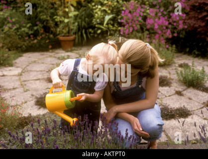 Kleinkind alt mit ihrer Mutter mit einer Gießkanne, Lavendel Pflanzen im Garten Wasser Stockfoto