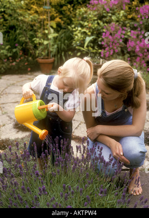 Kleinkind alt mit ihrer Mutter mit einer Gießkanne, Lavendel Pflanzen im Garten Wasser Stockfoto