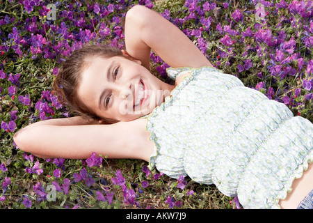 Lächelndes pre-teen Mädchen liegend, Arme hinter dem Kopf im Bereich der Blumen, Draufsicht Stockfoto