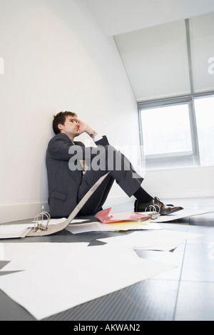 Betonte Geschäftsmann am Boden der leeren Büro von verstreuten Dateien Stockfoto