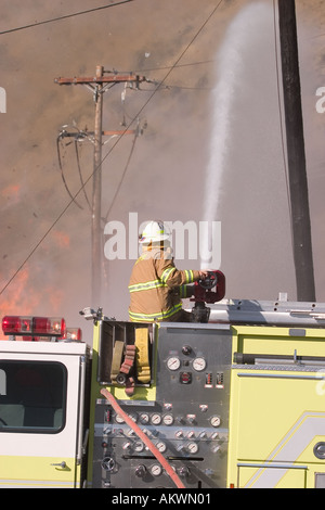 Wasser gesprüht auf einem großen industriellen Feuer von Nozel auf Feuerwehrauto mit Feuerwehrmann Stockfoto