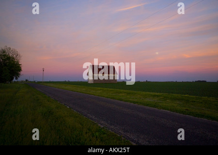 Sonnenuntergang und Mondaufgang über eine Scheune entlang einer Landstraße in Champaign County Illinois Stockfoto