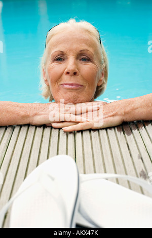 Deutschland, Senior Frau ruht am Rand des Pools, Lächeln Stockfoto