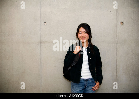 Lächelnde asiatische Universität College-Student gegen Betonmauer. Stockfoto