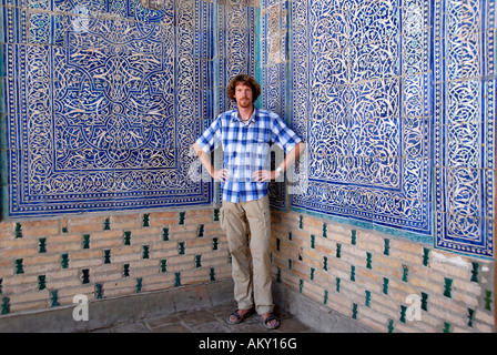 Junger Mann an fein dekorierte Wand mit blauen und weißen Kacheln und Zoroastrian Symbole der Leichtigkeit Tash Hauli Palast Khiva Uzbekistan Stockfoto