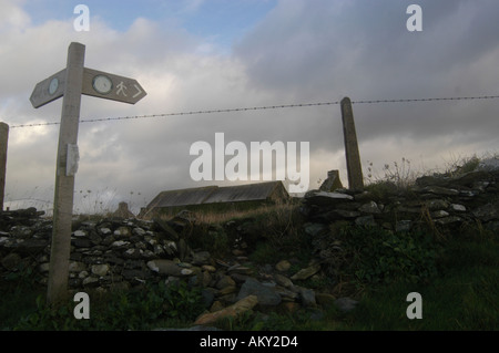 Verlassenes Haus hinter Feuerstein Trockenmauer mit Fußweg zu unterzeichnen, im Vordergrund im Cemlyn Bay in Anglesey, Nordwales Stockfoto