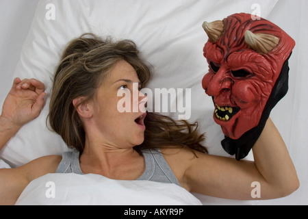 Frau im Bett liegend, Teufel Maske Stockfoto