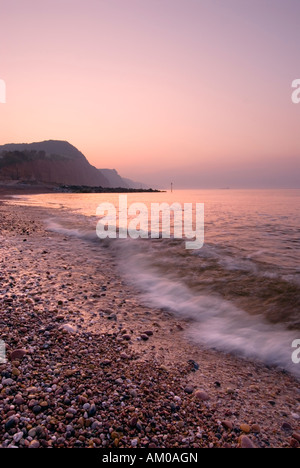 Rosa Sonnenaufgang über den Strand von Sidmouth mit Schiffswrack am Horizont Stockfoto