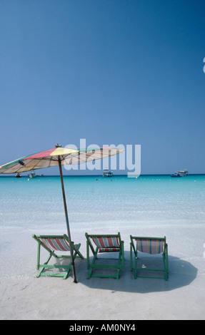 THAILAND Pattaya Coral Island Beach drei leere Liegestühle unter Dach am Rand des Wassers mit Boote vor Anker vor der Küste. Stockfoto