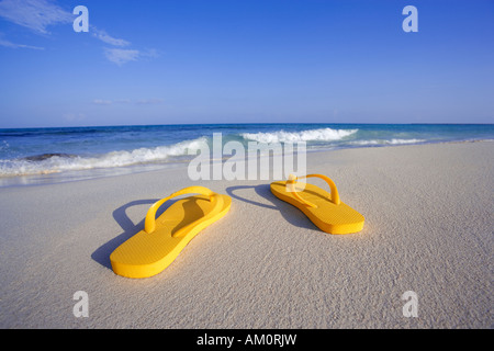 Paar gelb Flip flop Sandalen am Strand in der Nähe von Gewässerrand in Playa del Carmen, Mexiko Stockfoto