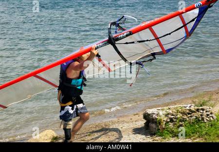 Ein älterer Mann trägt sein Windsurfbrett an die Küste in der Nähe der Niagarafälle in Ontario, Kanada, wo er einen Moment der Ruhe inmitten der mächtigen Kulisse bietet. Stockfoto