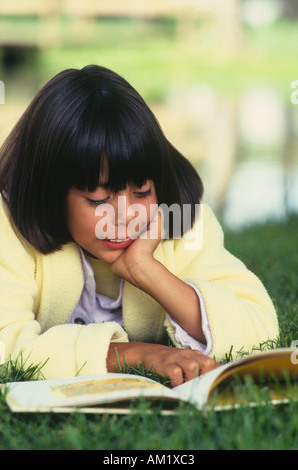 Mädchen liegend auf Bauch mit Kinn in Händen lesen buchen im park Stockfoto