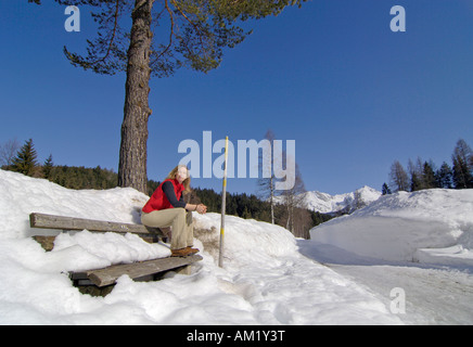 Frau sitzt auf einer Holzbank in der tief verschneiten Landschaft, Leutasch, Tirol, Österreich Stockfoto