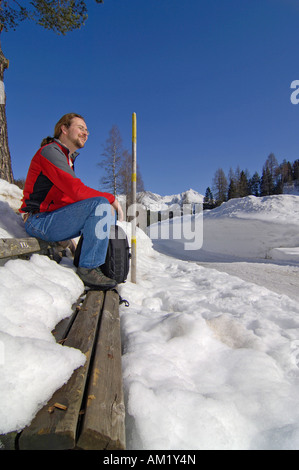 Mann sitzt auf einer Holzbank in der tief verschneiten Landschaft, Leutasch, Tirol, Österreich Stockfoto