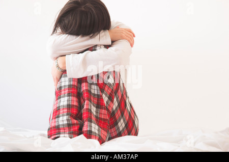 Frau trägt Pyjama sitzt auf Bett Stockfoto