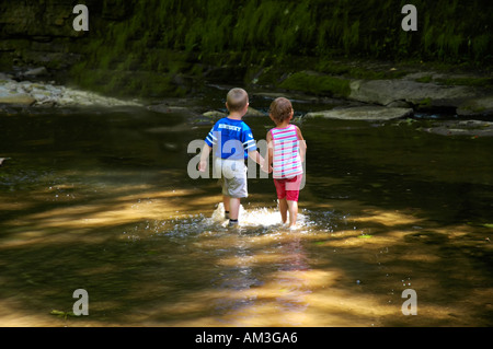 Jungen und Mädchen Hand in Hand und in einem Bach waten Stockfoto