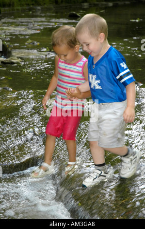 Jungen und Mädchen Hand in Hand und in einem Bach waten Stockfoto