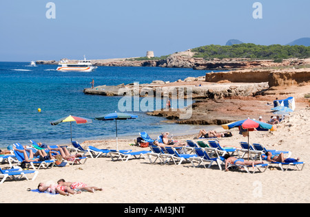 Touristen am Strand von Platges de Comte, Ibiza mit der Fähre in der Ferne Stockfoto