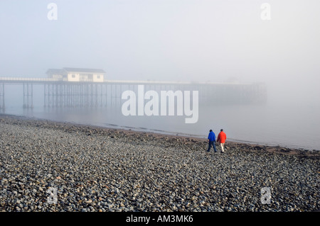 Penarth Pier, South Wales an einem nebligen Tag. Ein paar in blaue und rote Schichten sind am Kiesstrand entfernt. Stockfoto